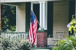 front porch with white pillars and a brick foundation and an American flag