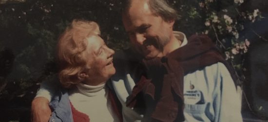 two older white adults, their arms around each other, looking into each others eyes and smailing