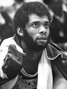 Black and white photo of a very young Kareem Abdul-Jabbar in 1975, he is looking up attentively, he has a towel around his neck.